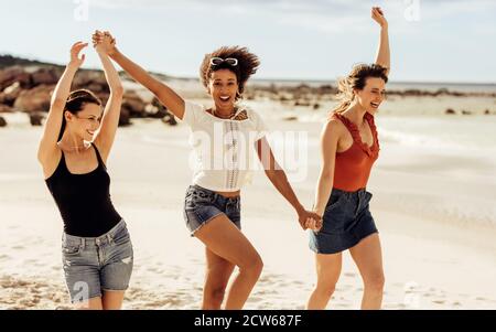 Junge Frauen gehen am Strand in einer verspielten Stimmung. Multiethnische Freundinnen auf einem Strandurlaub Spaß haben. Stockfoto