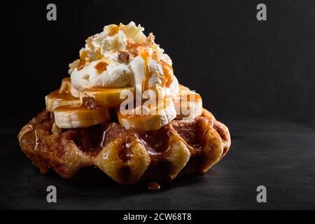 Waffeln mit Bananen garniert mit Karamellsirup auf einem dunklen Steinhintergrund Stockfoto