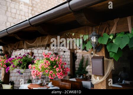 Ein brauner Briefkasten unter einer Straßenlampe auf einer Holzstruktur bei einem Pavillon mit hängenden Blumentöpfen und Tischen und Stühlen. Stockfoto