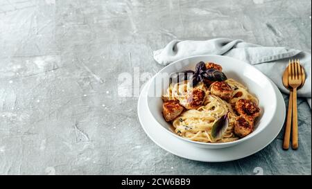 Zucchini Parmesan Fleischbällchen mit Pasta Carbonara in weißer Platte auf grauem Hintergrund. Nahaufnahme von cremigem Carbonara mit Kopierraum links Stockfoto