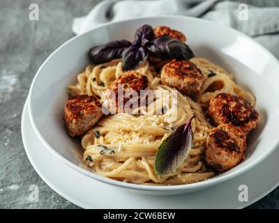 Zucchini Parmesan Fleischbällchen mit Pasta Carbonara in weißer Platte auf grauem Hintergrund. Nahaufnahme von cremigem Carbonara mit Kopierraum links Stockfoto