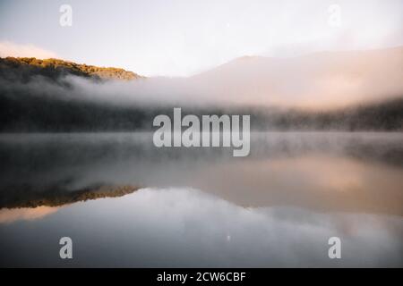 Neblige Seenlandschaft und lebendige Herbstfarben in Bäumen bei erstaunlich nebligen Sonnenaufgang.Sfanta Ana, Rumänien, Siebenbürgen. Stockfoto