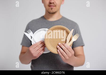 Kunststoff vs nachhaltige Essgeschirr Auswahlkonzept - Kunststoff und Holz Und Papier Einweg-Utensilien in männlichen Händen über grau Hintergrund Stockfoto