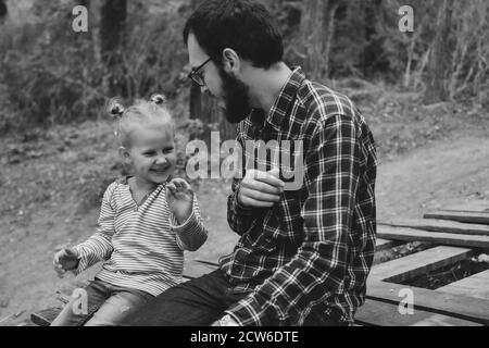 Baby und Vater spielen im Herbstpark. Vater und Tochter sitzen draußen auf einer Holzbrücke. Glückliche Familienmomente der Kindheit. Stockfoto