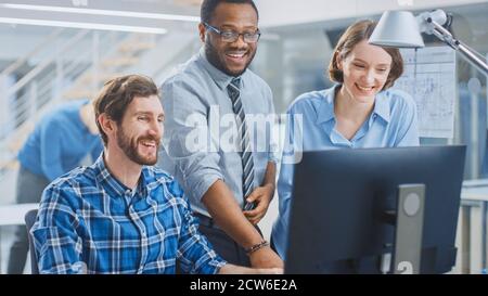 In der Industrial Engineering Facility: Männlicher Ingenieur, der am Desktop-Computer arbeitet, weiblicher leitender Ingenieur und Projektmanager beenden das Projekt Stockfoto