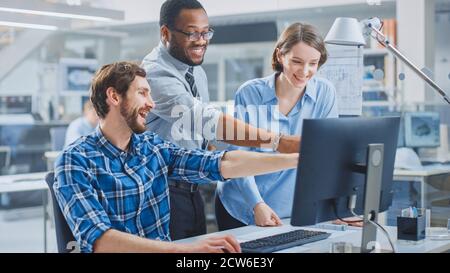 In der Industrial Engineering Facility: Männlicher Ingenieur, der am Desktop-Computer arbeitet, weiblicher leitender Ingenieur und Projektmanager diskutieren und erklären Stockfoto