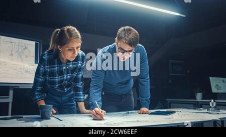 In der dunklen Industrial Design Engineering Facility männlich und weiblich Ingenieure sprechen und arbeiten an einem Blueprints mit Digital Tablet Und Konferenztisch Stockfoto