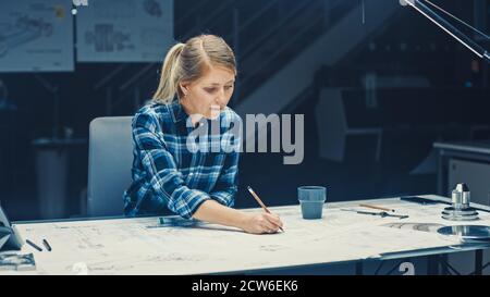 Weibliche Ingenieurin sitzt an ihrem Schreibtisch arbeitet mit Blueprints Laying on a Table, verwendet Bleistift, Lineal und Digital Tablet. Im dunklen Industriedesign Stockfoto