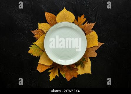 Herbst und Thanksgiving Tagestisch Einstellung mit gefallenen Blättern und Leere weiße Platte auf dunklem Hintergrund Stockfoto