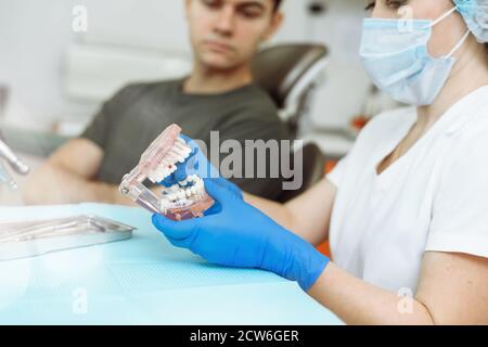 Zufriedener Patient auf dem Zahnarztstuhl. Zahnarzt, der dem Patienten in der Klinik künstliche Zähne erklärt. Mann, der in der Zahnklinik zu Besuch ist. Stockfoto