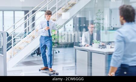 Im hellen Firmenbüro fährt der coole Geschäftsmann mit Krawatte und Hemd Skateboard durch den Büroflur. Im Hintergrund Professional People Stockfoto