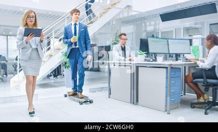 Im hellen Firmenbüro fährt der coole Geschäftsmann mit Krawatte und Hemd Skateboard durch den Büroflur. Im Hintergrund Professional People Stockfoto