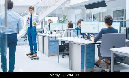 Im hellen Firmenbüro fährt der coole Geschäftsmann mit Krawatte und Hemd Skateboard durch den Büroflur. Im Hintergrund Professional People Stockfoto