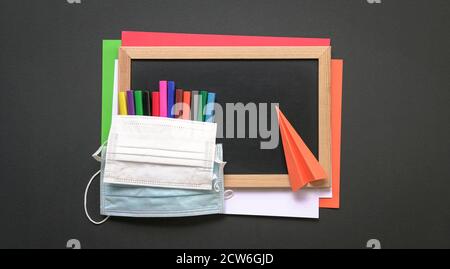 Gesichtsmaske auf schwarzem Brett und farbigen Papieren mit magischen Farbstiften und Papierebene. Draufsicht. Stockfoto