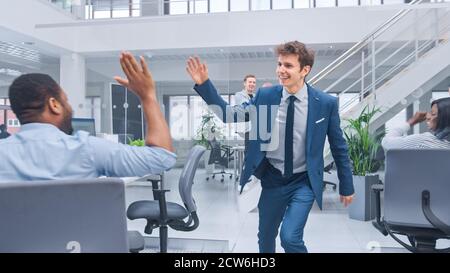 Junge glückliche Geschäftsführerin in Anzug und Krawatte Tanzen und Hochfives im Büro geben. Erfolg Wird Gefeiert. Vielfältiges und motiviertes Business Stockfoto
