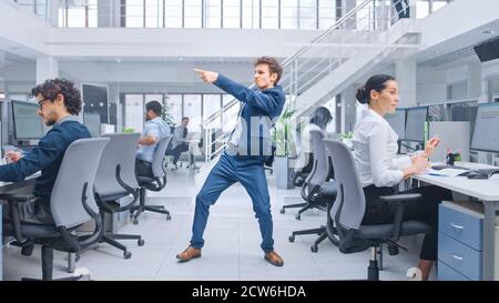 Junger, fröhlicher und gutaussehender Geschäftsleiter in Anzug und Krawatte, der im Büro tanzte. Vielfältige und motivierte Geschäftsleute arbeiten daran Stockfoto
