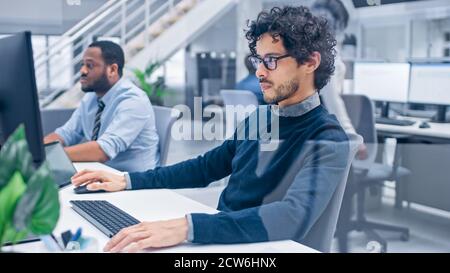 Young Handsome Manager mit Curly Hair arbeitet auf einem Desktop-Computer und vergleicht Daten mit einer Software. Vielfältige und motivierte Geschäftsleute arbeiten daran Stockfoto