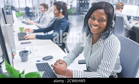 Schöne junge weibliche Customer Service Operator Lächeln für ein Porträt In einem geschäftigen, modernen Call Center mit einem multikulturellen Team Des Büros Stockfoto