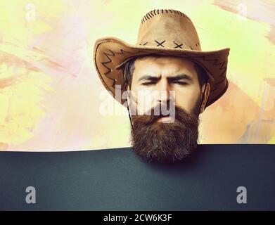 Bärtiger Mann, langer Bart. Brutal kaukasisch lustig unrasiert Hipster in vintage Cowboy Hut mit blauem Papier Blatt im Studio auf bunten Hintergrund Stockfoto