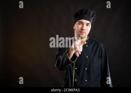 Porträt eines jungen Mannes in einem schwarzen Koch Anzug gekleidet Dabei beobachte ich dich, wie du auf einem Braun posierst Hintergrund mit Kopierraum Werbefläche Stockfoto