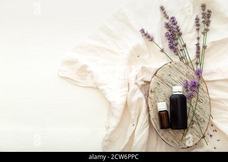 Lavendel ätherisches Öl Flaschen auf weißem Holz rustikalen Tisch mit Stoff, frische Lavendelblüten. Aromatherapie-Behandlung, natürliche Spa-Kosmetik Stockfoto