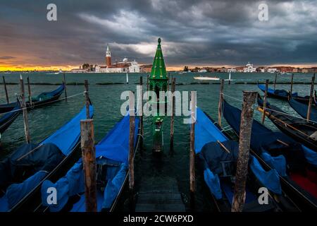 Ein klassischer Votivschrein in der Lagune von Venedig steht nach einem Sturm unter Gondeln. Stockfoto