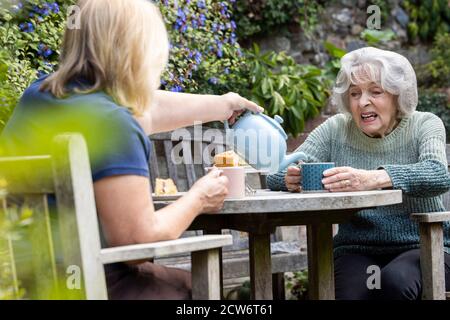 Ältere Frau Besucht Einsame Ältere Mutter Im Garten Während Der Sperre Stockfoto