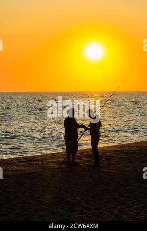 Zwei Fischer stehen am Strand bei Sonnenuntergang in West Bexington, einem Dorf im Südwesten von Dorset, England, gelegen hinter Chesil Beach in der Nähe von Bridport Stockfoto