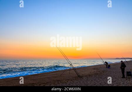 Angelruten und Sonnenuntergang am Strand von West Bexington, einem Dorf im Südwesten von Dorset, England, gelegen hinter Chesil Beach in der Nähe von Bridport, bei Sonnenuntergang Stockfoto