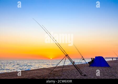 Angelruten bei Sonnenuntergang am Strand von West Bexington, einem Dorf im Südwesten von Dorset, England, gelegen hinter Chesil Beach in der Nähe von Bridport Stockfoto