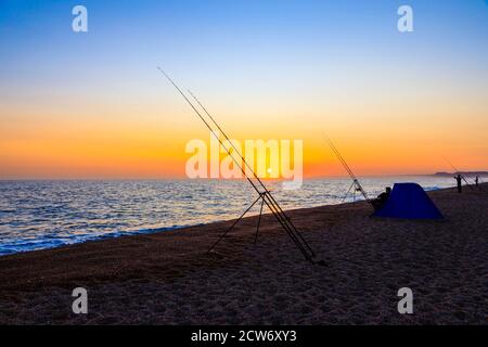 Angelruten und Sonnenuntergang am Strand von West Bexington, einem Dorf im Südwesten von Dorset, England, gelegen hinter Chesil Beach in der Nähe von Bridport, bei Sonnenuntergang Stockfoto