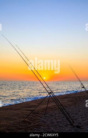 Angelruten und Sonnenuntergang am Strand von West Bexington, einem Dorf im Südwesten von Dorset, England, gelegen hinter Chesil Beach in der Nähe von Bridport, bei Sonnenuntergang Stockfoto