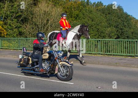 Motorradfahrer, die Pferde überholen; Reiter, die orangefarbene, gut sichtbare Kleidung am Straßenrand tragen als klassische Motorradpässe, Tierverkehr in Manchester, Großbritannien Stockfoto