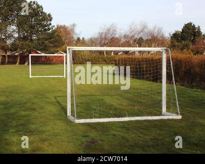 Zwei weiße hölzerne Fußball-Torpfosten auf einem Rasen, mit Häusern im Hintergrund. Stockfoto