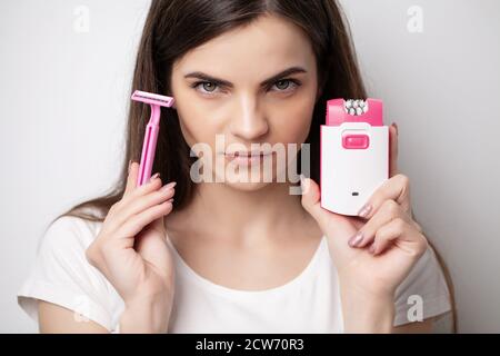 Eine Frau verwendet einen Epilierer und Rasierer, um Haare zu entfernen Stockfoto