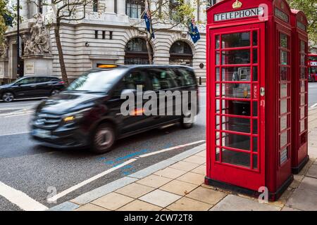 Iconic London - ein Mercedes Vito London Taxi fährt an zwei traditionellen roten Telefonzellen im Zentrum von London vorbei. Bewegungsunschärfe der Taxibewegung. Stockfoto