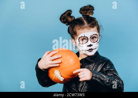 Nahaufnahme Porträt von Zombie kleines Mädchen isoliert auf blauem Studio Hintergrund halten Orang Kürbis, trägt kreative Make-up, feiert Halloween-Urlaub oder Stockfoto