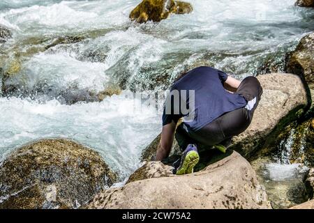 Tourist guy in Sportbekleidung zieht Wasser aus einem stürmischen Berg Fluss Stockfoto