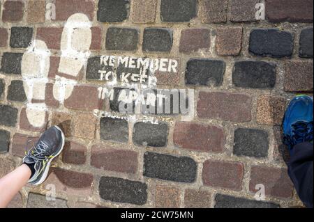 LONDON - 14. SEPTEMBER 2020: Füße gehorchen einem sozialen Distanzierungszeichen auf alten Ziegelboden am Camden Market während der Covid 19 Pandemie gemalt Stockfoto