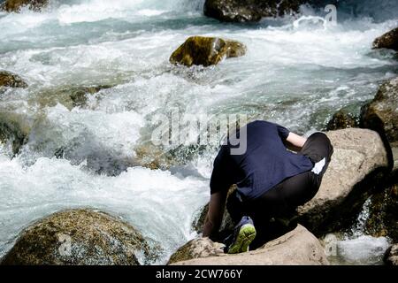 Tourist guy in Sportbekleidung zieht Wasser aus einem stürmischen Berg Fluss Stockfoto