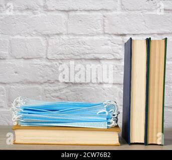 Stapel von verschiedenen Büchern und Einweg-medizinische Masken auf weißem Hintergrund, Konzept des Besuchs Bibliotheken in persönlichen Schutzausrüstung während quara Stockfoto