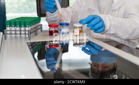 Forscher im Labor. Farbige Flüssigkeiten in Flaschen und grünen Reagenzgläsern. Glänzendes Analysenglas mit Reflexion des Laborassistenten mit einer Spritze in der Hand. Stockfoto