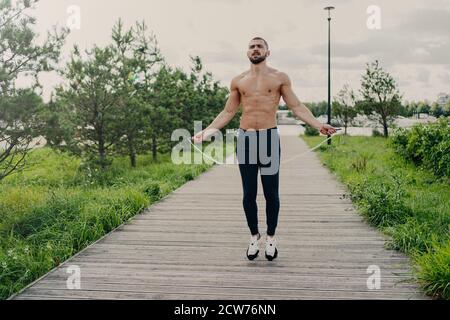 Sportlich muskulös Mann nutzt Springseil für Cardio-Training im Freien, hat perfekten Körper, atmet frische Luft und zeigt Ausdauer, arbeitet sich selbst de Stockfoto