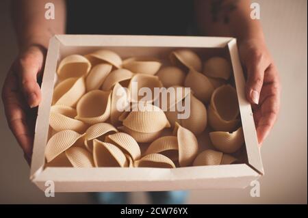 Frau hält Papierbox voll von handgefertigten Abissini Pasta Nahaufnahme. Draufsicht. Selektiver Fokus. Traditionelle italienische Küche. Glutenfrei. Stockfoto