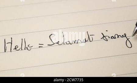 Anfänger Indonesisch Sprache Lernender schreiben Hallo formelles Wort Selamat siang Für Hausaufgaben auf einem Notebook-Makrofoto Stockfoto