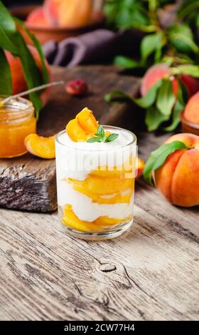Pfirsichfrucht Dessert in Glas Tasse auf Holztisch. Hausgemachtes Dessert mit Früchten. Obstsalat mit Joghurt oder Sauerrahm. Stockfoto