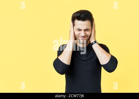 Hübscher Mann, der seine Ohren mit Händen bedeckt, die Angst haben, schlechte Nachrichten auf gelbem Hintergrund isoliert zu hören Stockfoto