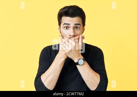 Schockierter Mann, der den Mund mit Händen über gelbem Hintergrund bedeckt. Emotionen und geheimes Konzept Stockfoto