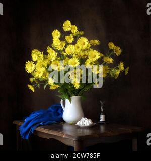 Frühling Stillleben gelb Gänseblümchen Studie mit blauem Schal und Weiße Kanne Stockfoto