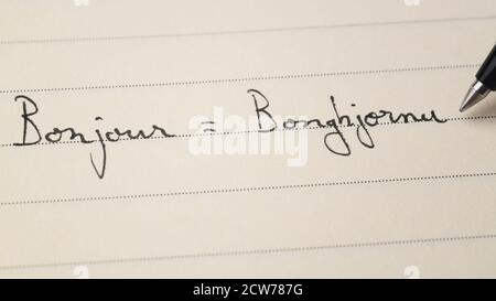 Anfänger korsische Sprache Lerner schreiben Hallo Wort Bonjour auf Französisch Und Bonghjornu auf Korsika für Hausaufgaben auf einem Notebook-Makro Aufnahme Stockfoto